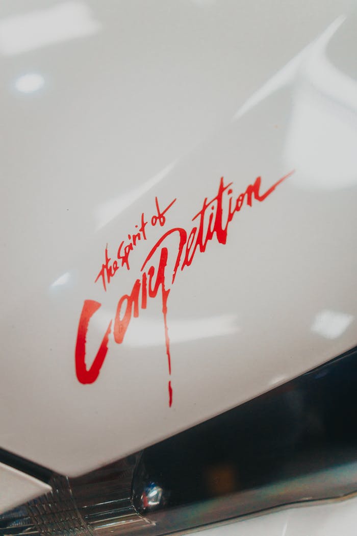 Close-up shot of car hood decal reading 'The Spirit of Competition' with a shiny finish.
